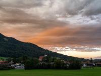 Orange leuchtende Abendwolkenwand und Wolkenstreifen über Aschau und Aschauer Berg